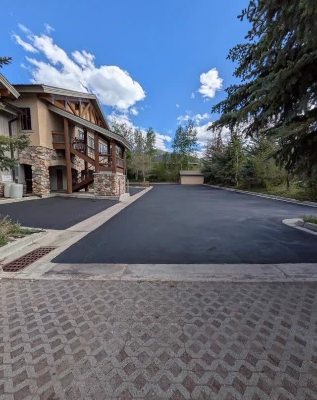 Driveway and lodge entrance with stone facade, dark pavement, trees, and a blue sky with clouds