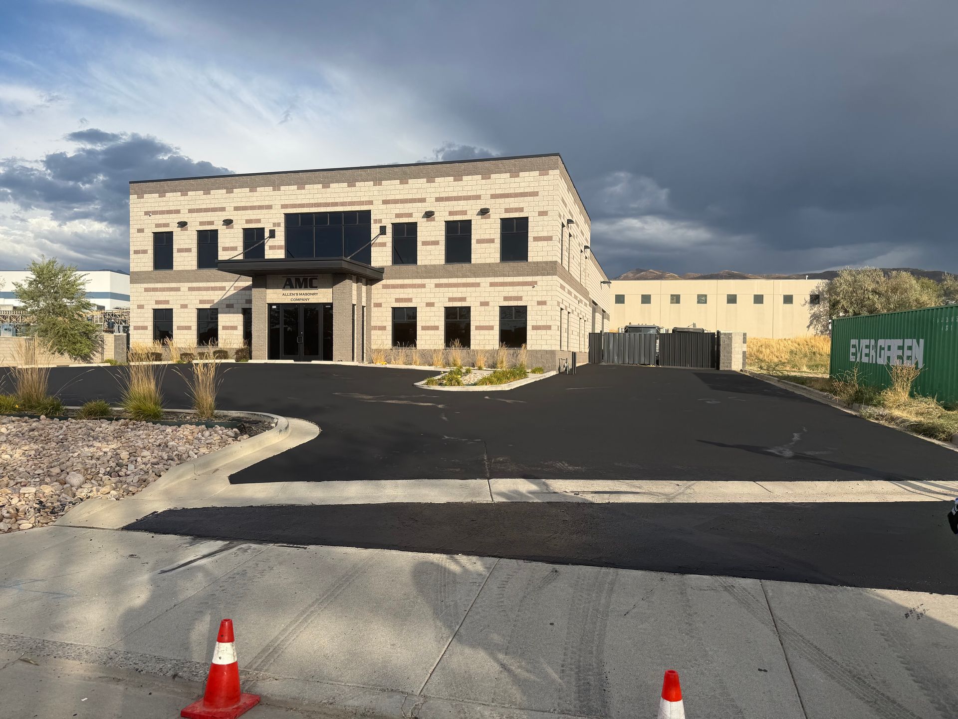 Partially finished two-story building with black driveway and orange traffic cones under cloudy sky
