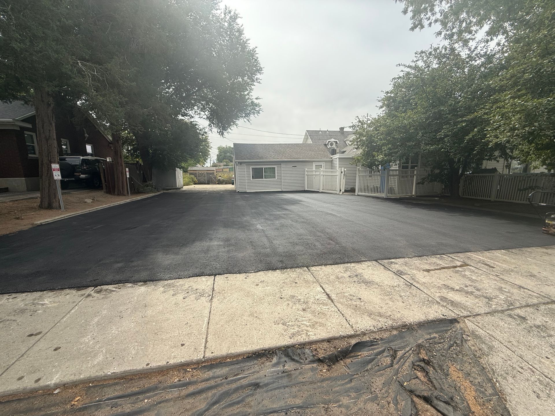 Freshly paved driveway leading to a white building, framed by trees and a concrete curb