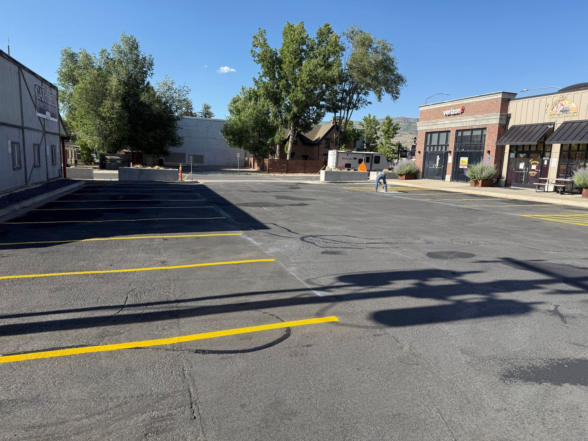 Empty parking lot with yellow lines beside low buildings and trees in bright sunlight