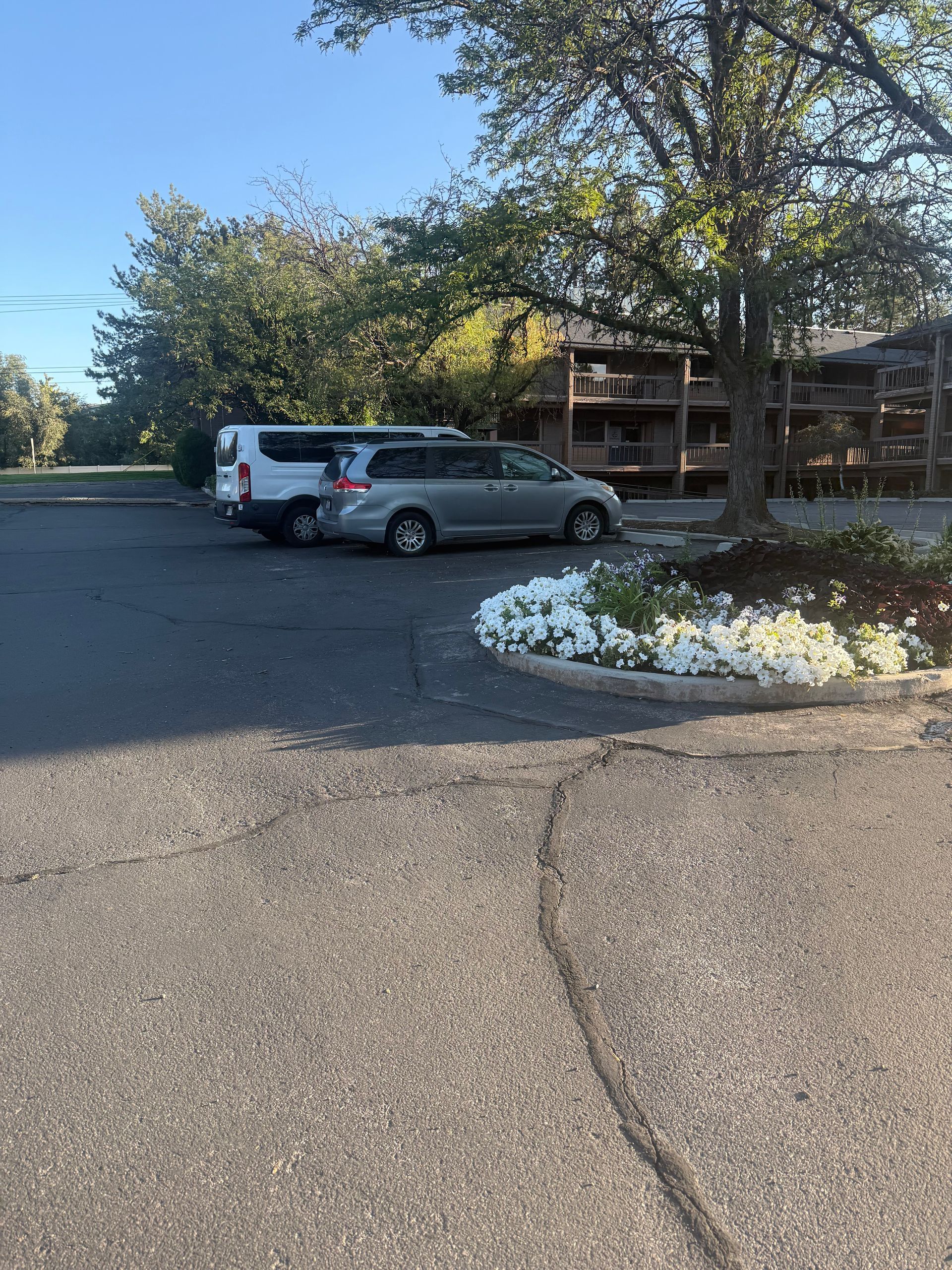Parking lot with two parked vehicles beside a flower bed and a building in the background.