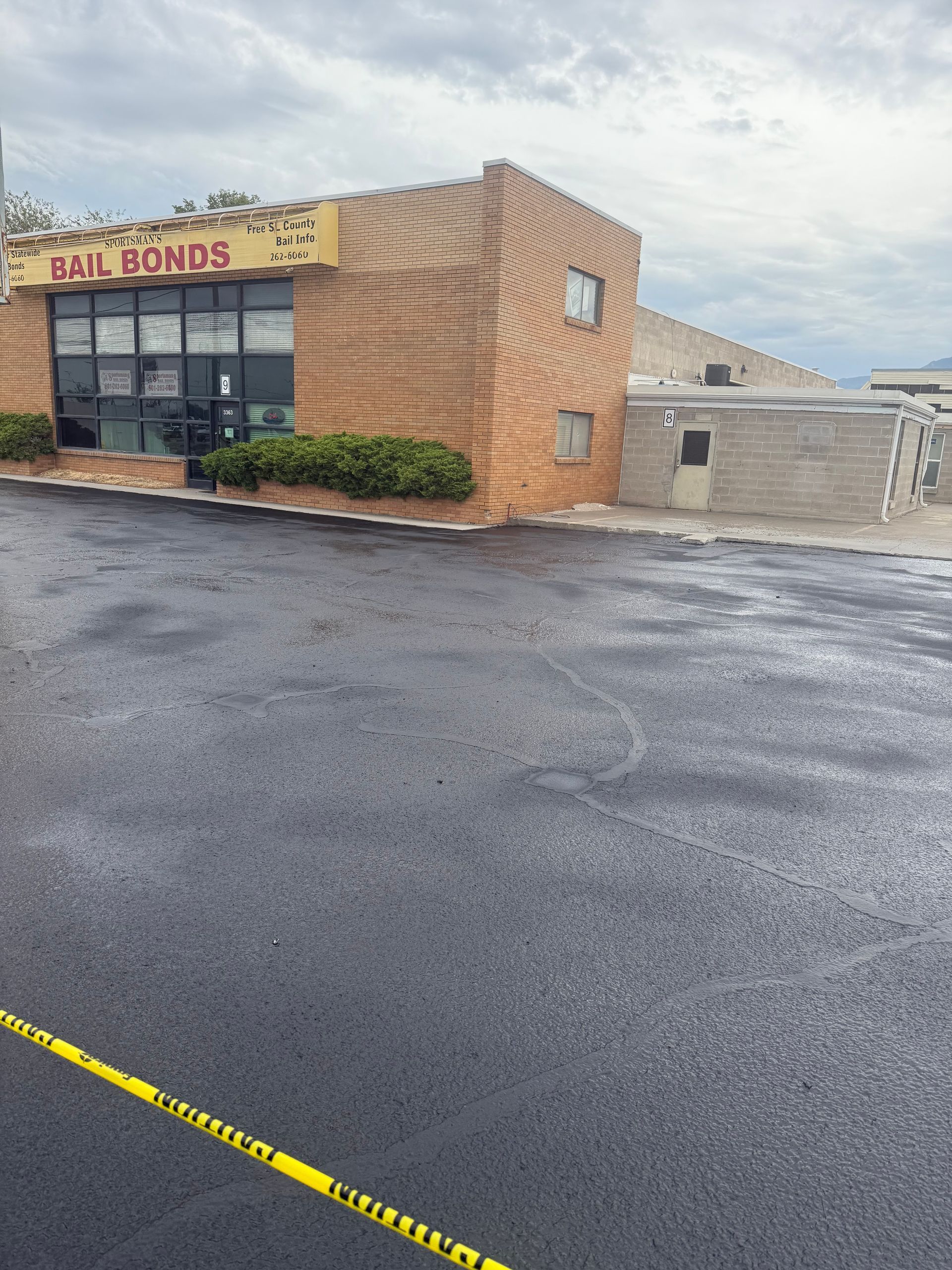 Storefront with tan brick exterior, yellow sign, and empty wet parking lot under cloudy sky