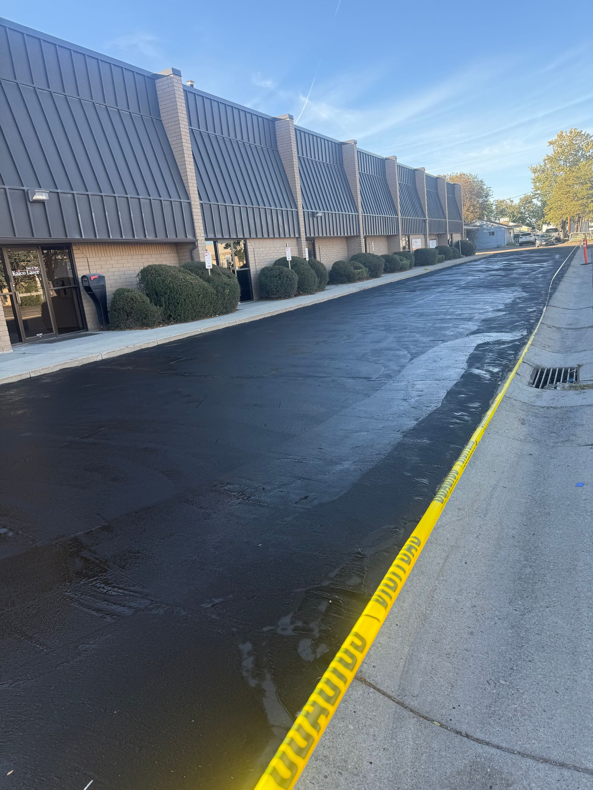 Freshly paved black road beside a building with a yellow caution tape line along the curb.