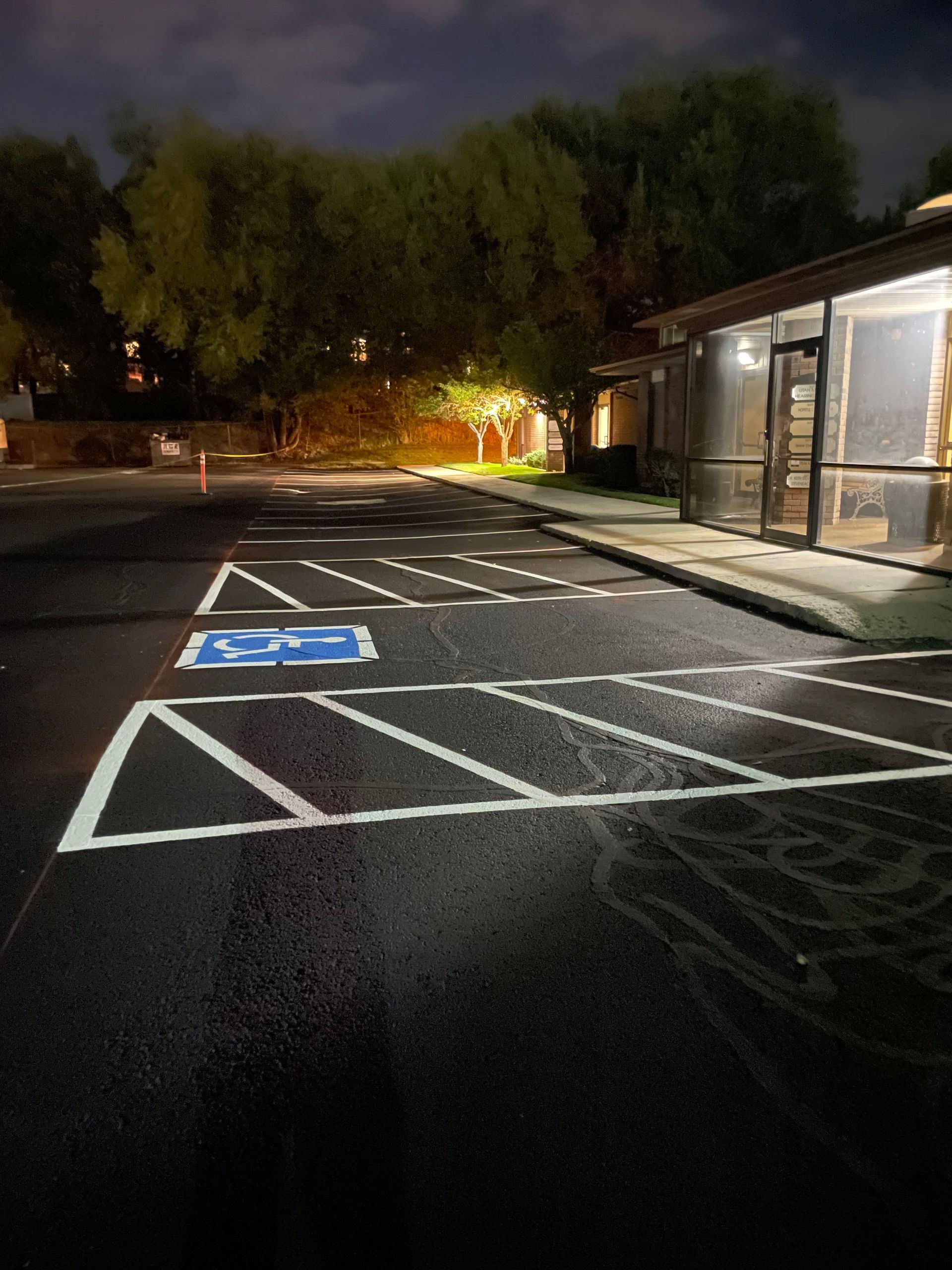 Nighttime parking lot with marked accessible parking spaces beside a lit building and trees.