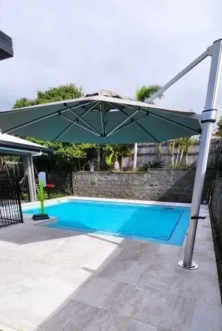 A Swimming Pool With A White Umbrella On Top In The Backyard — Doug Allen Pools In Beaconsfield, QLD