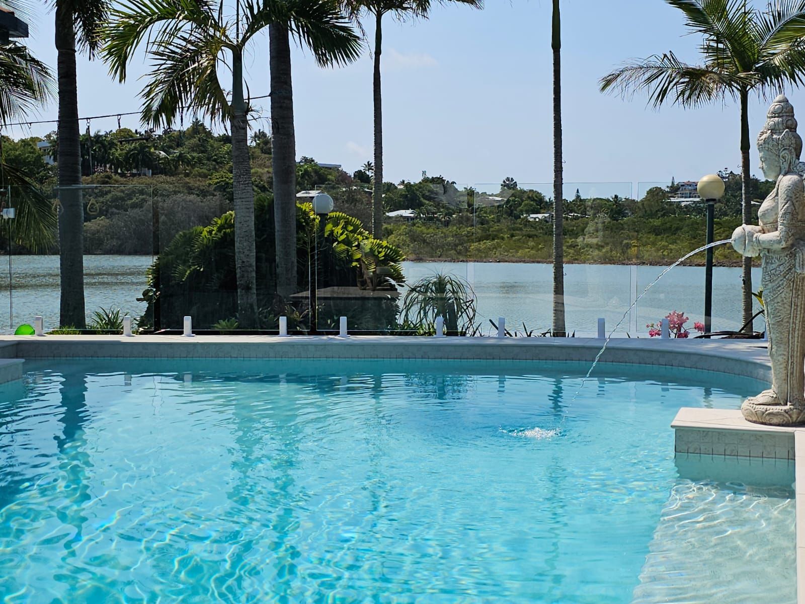 Resort pool with palm trees and a lake view on a sunny day — Doug Allen Pools In Beaconsfield, QLD