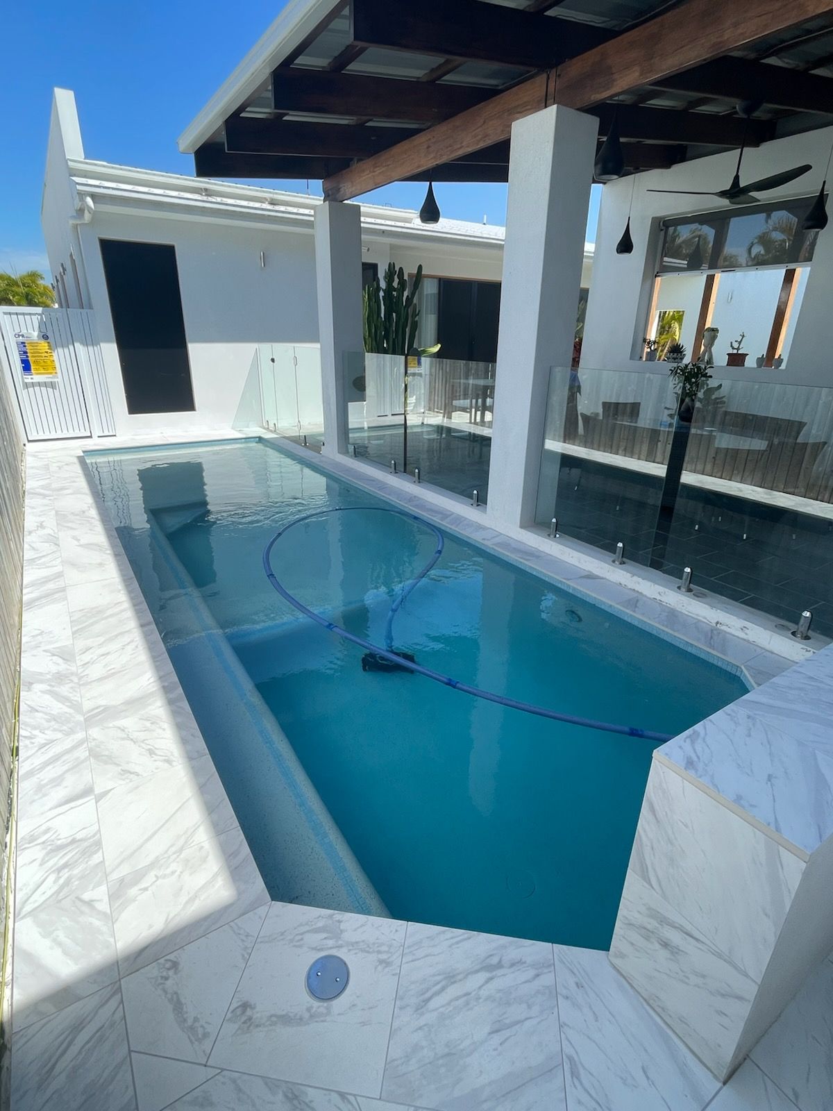 Small blue-tiled pool beside a white patio with glass walls and a covered outdoor seating area — Doug Allen Pools In Beaconsfield, QLD