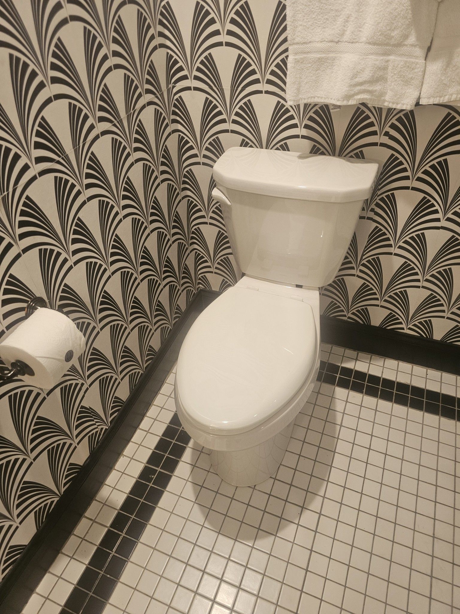 Small bathroom with a white toilet, patterned black-and-white wallpaper, and tiled floor.
