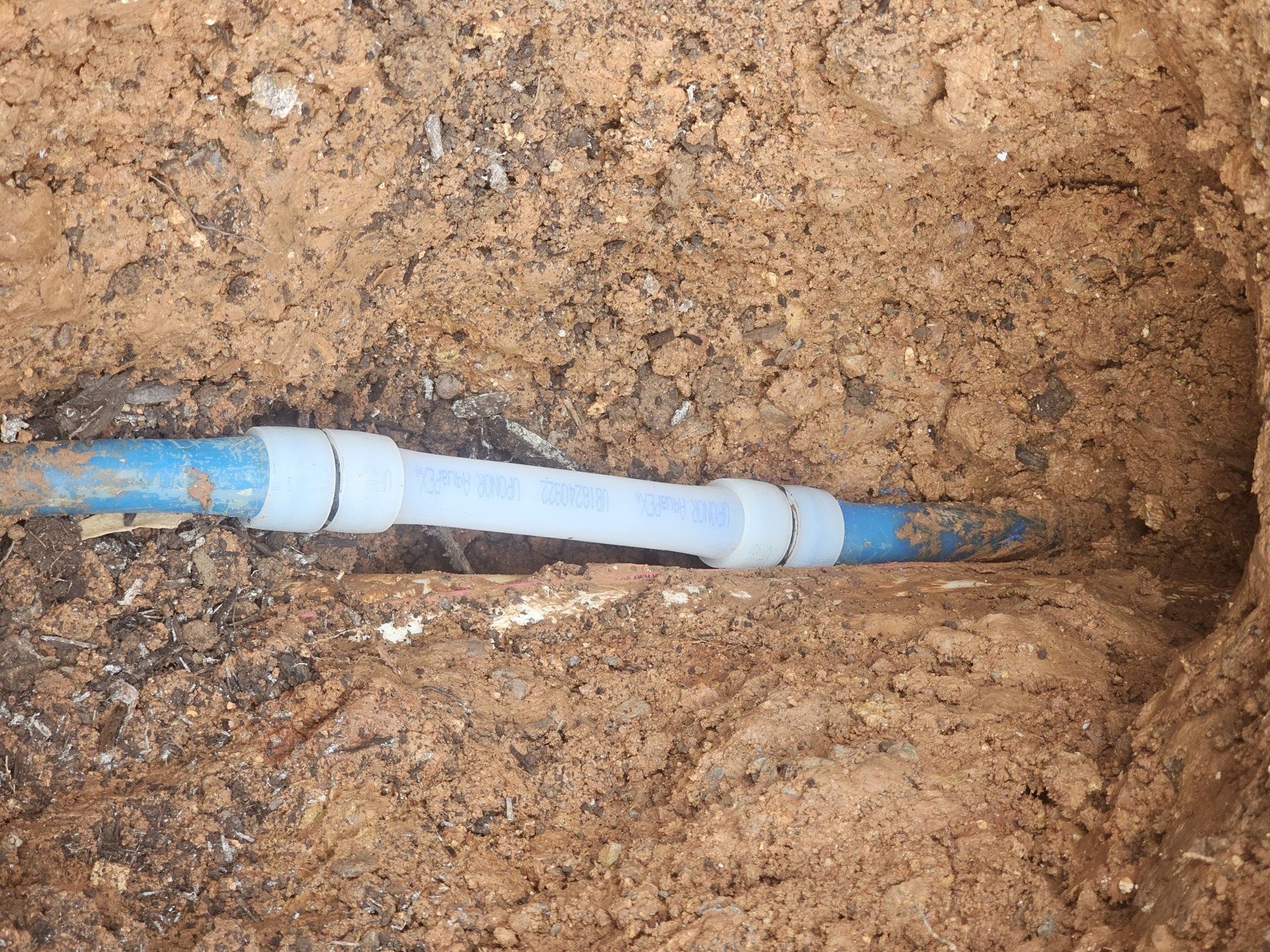 Blue PVC pipe joint in a dirt trench with soil packed around it