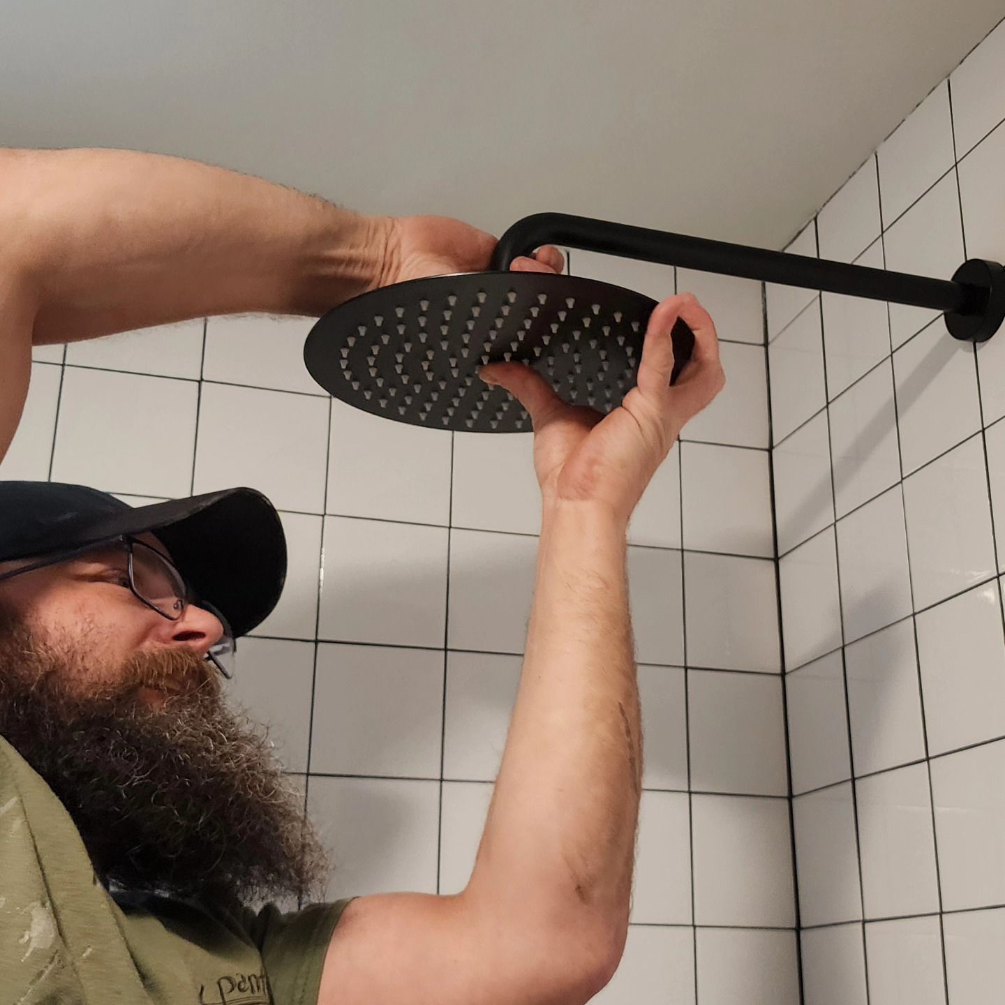 Man installing a black showerhead in a white tiled shower stall