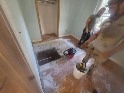 Workers removing carpet and flooring in a small room during renovation