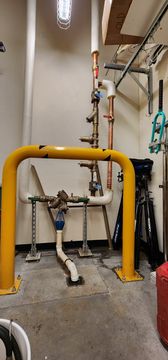 Yellow gas pipe in a mechanical room with exposed plumbing and valves on the wall