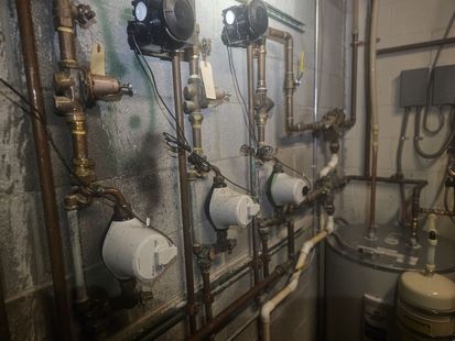 Boiler room wall with pipes, valves, gauges, and pumps in an industrial mechanical setup