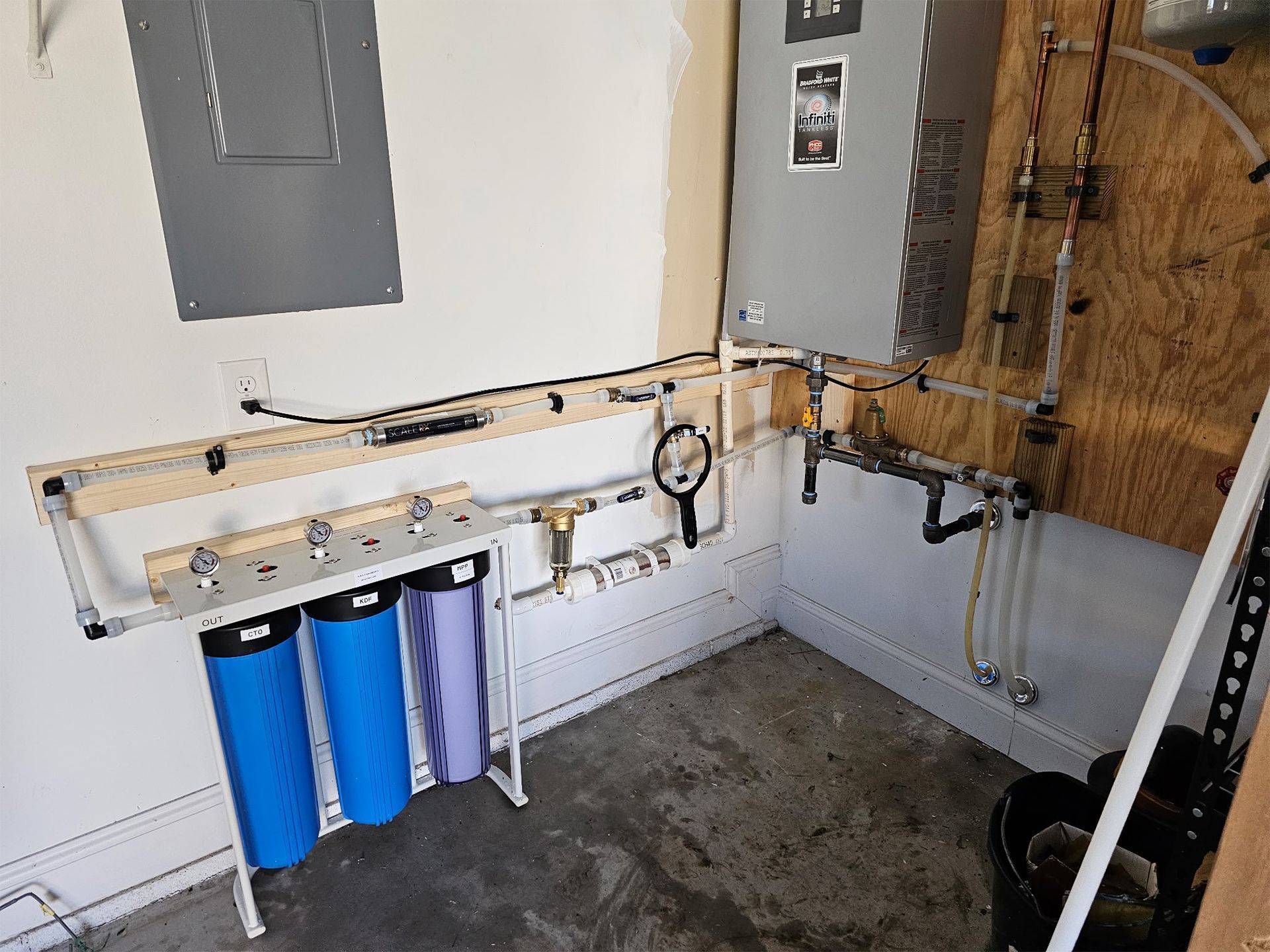 Plumbing and filtration system with blue and purple cylinders mounted on a wall in a utility room