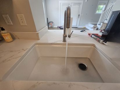 Kitchen sink with running faucet and white countertop, with a small cup on the left side.