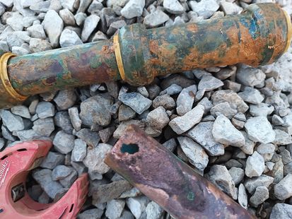Rusty metal pipe sections on gray gravel, with an orange ring and a red broken piece nearby