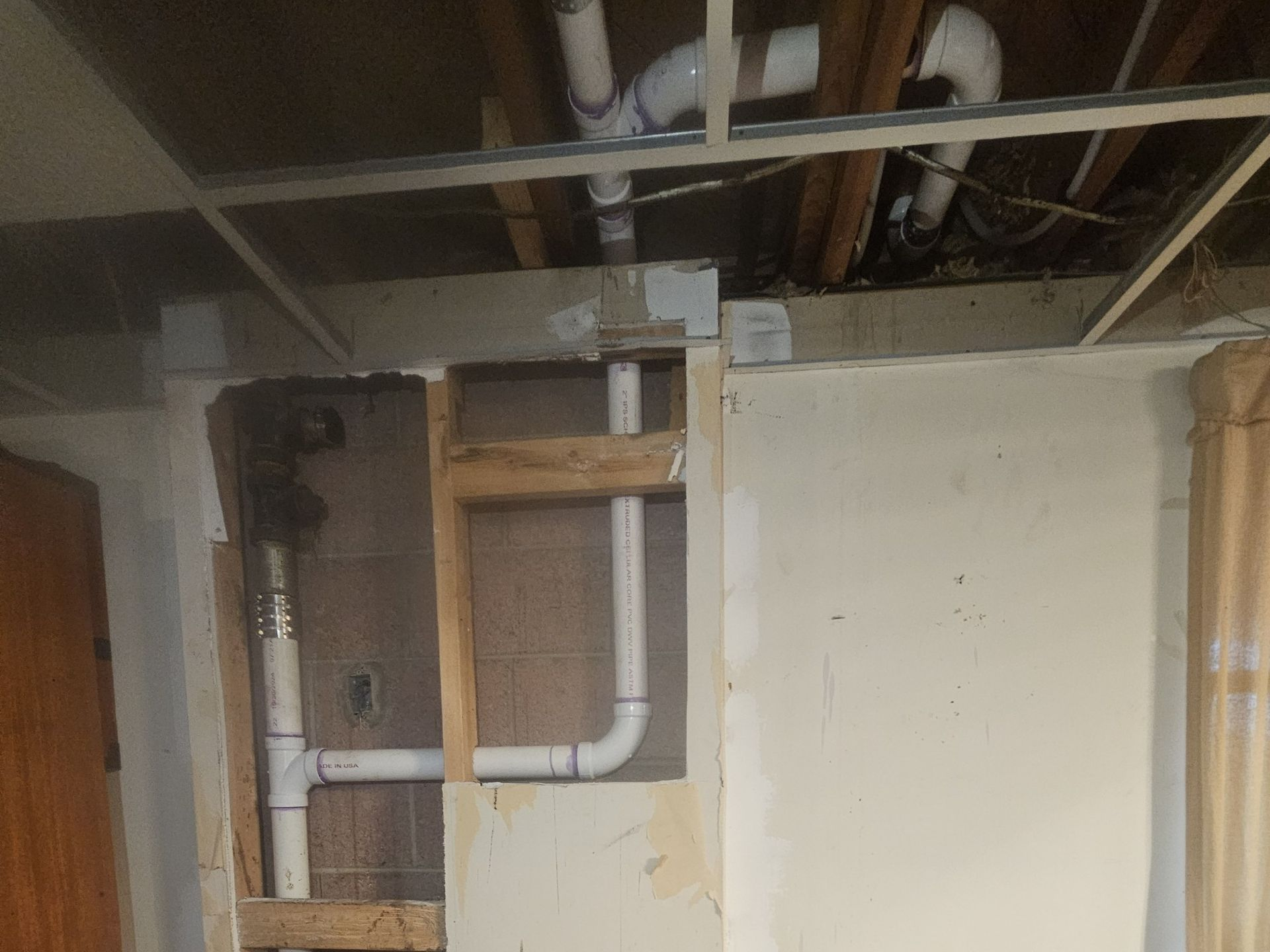 Partially open wall showing exposed pipes, beams, and wiring in an unfinished interior space