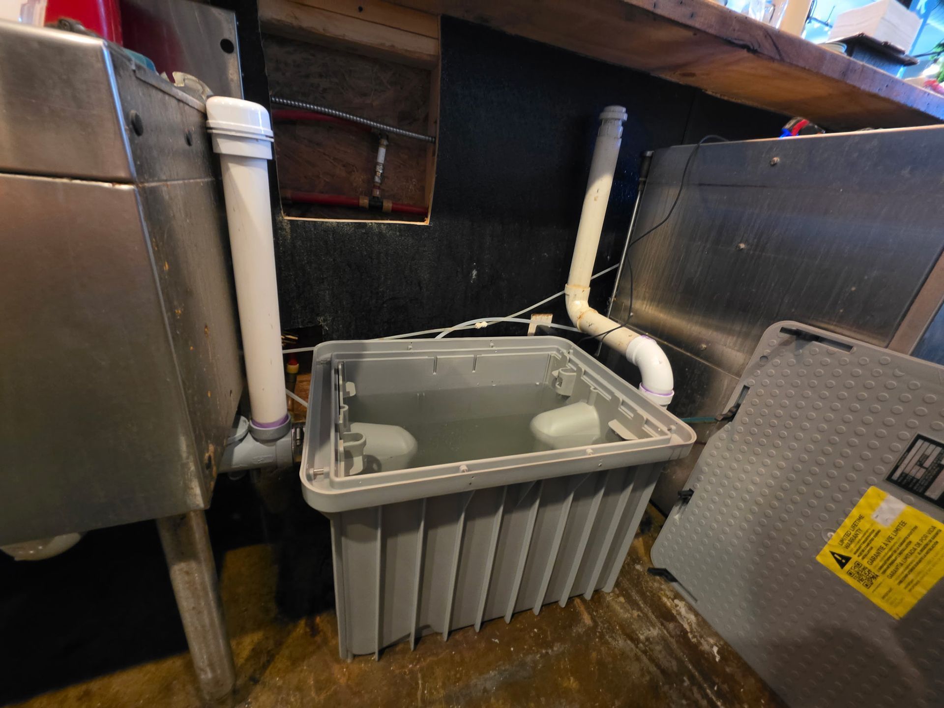 Gray utility sump basin with PVC pipes under a sink or basement floor.