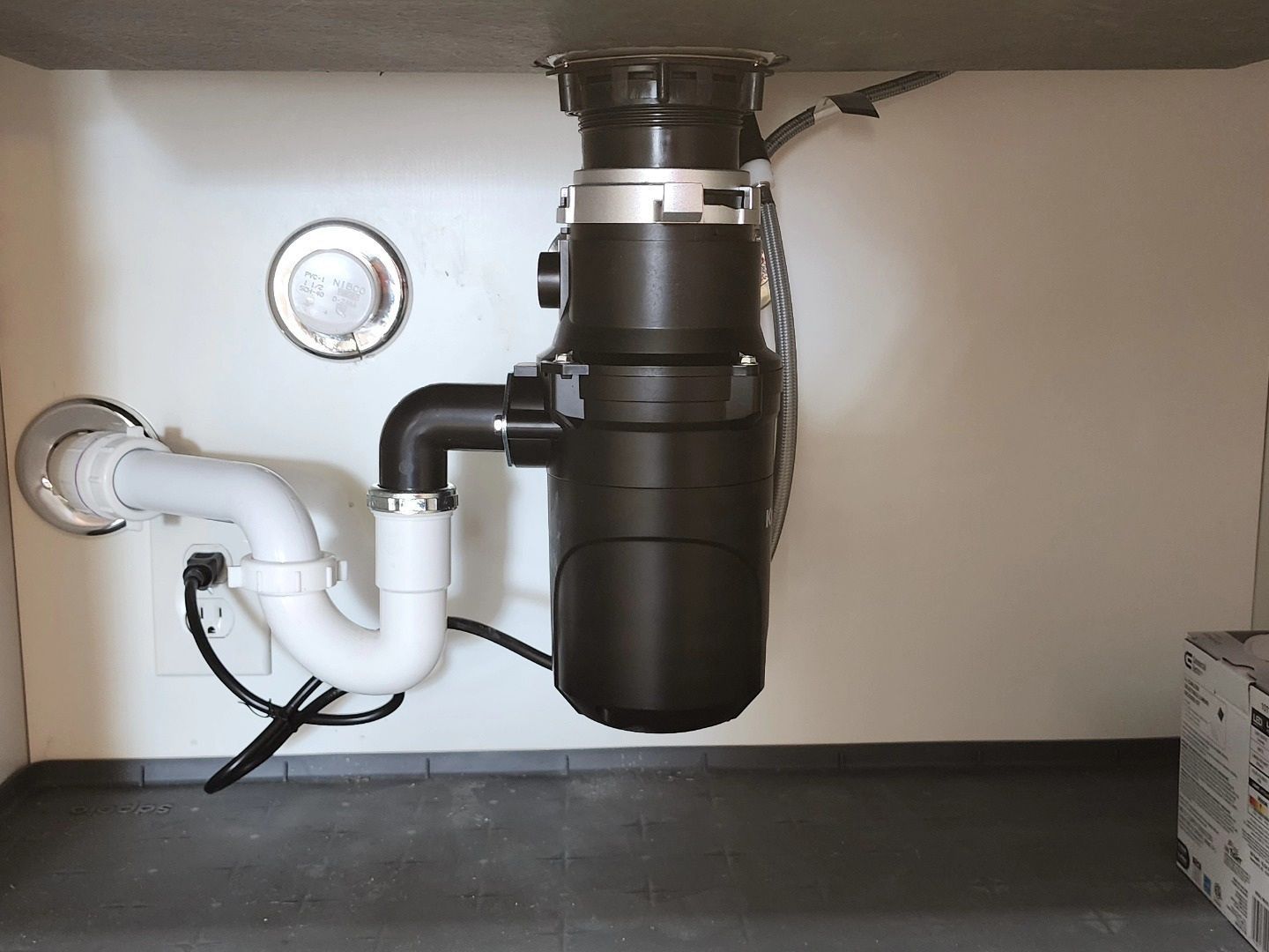 Under-sink plumbing with white and black drain pipes and a garbage disposal unit