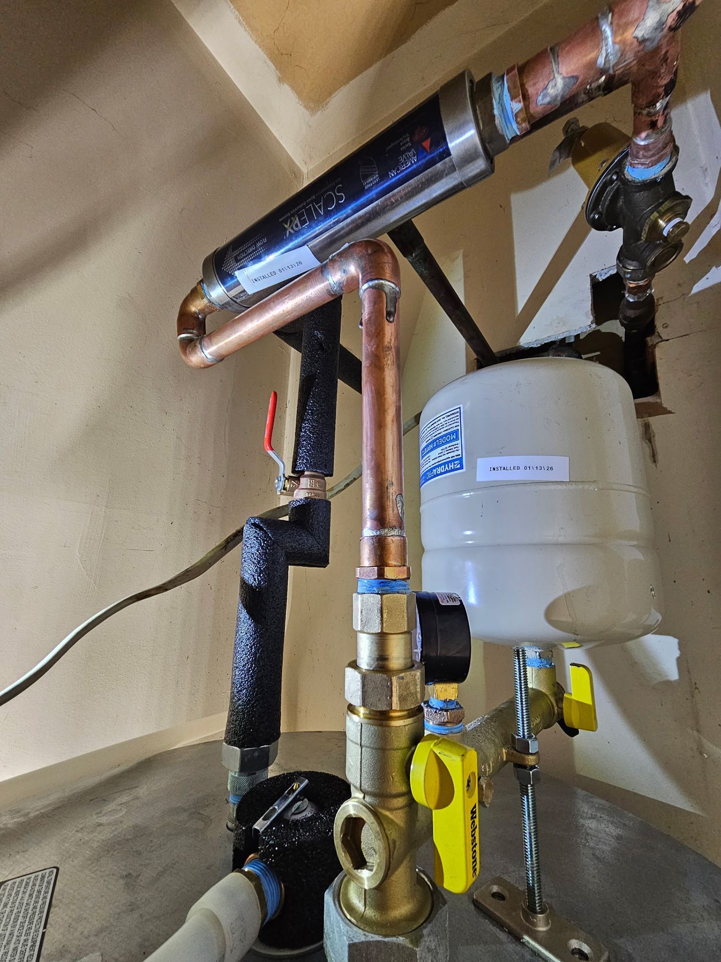 Copper plumbing pipes and a yellow-handled valve beside a white water heater in a utility area