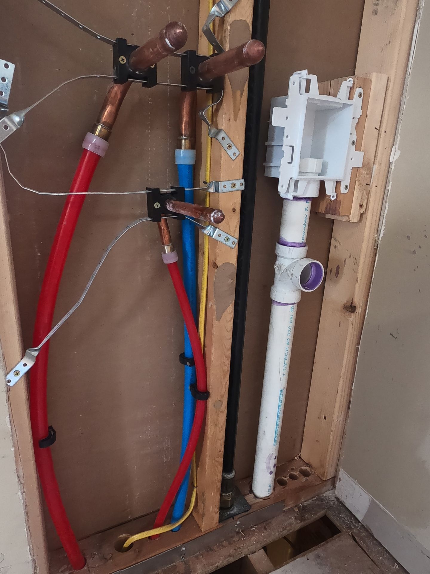 Exposed plumbing in a wall cavity with red and blue pipes and a white toilet tank assembly.