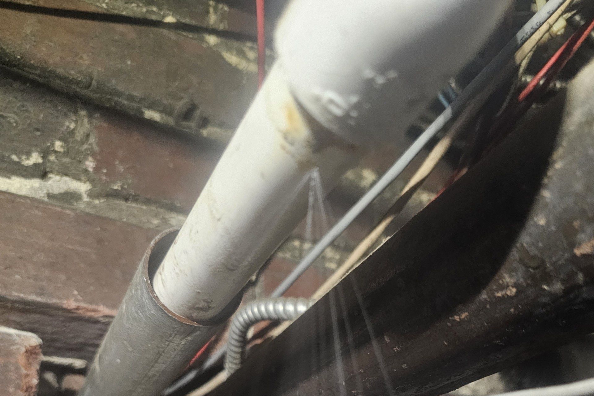 Close-up of white PVC pipes and wires against a dirty wooden wall and dark surface