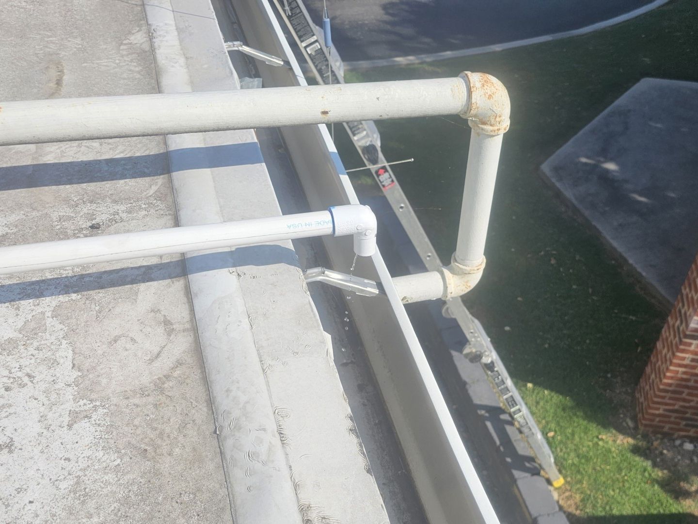 White PVC pipes run along a concrete edge beside dark water and a patch of grass.