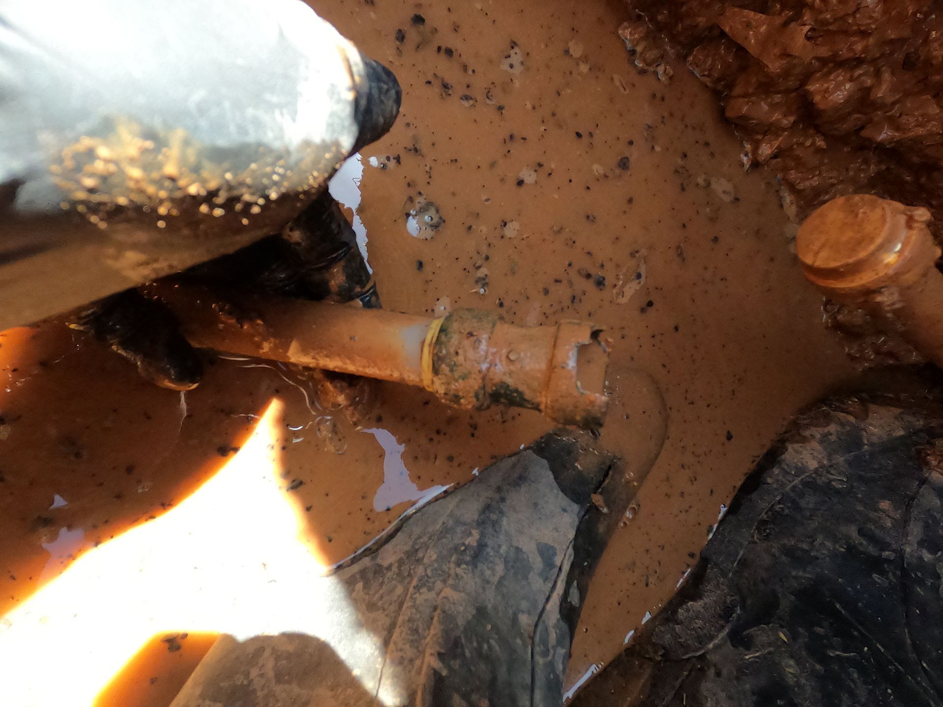 Close-up of muddy water with a rusty pipe and a person’s hand reaching in near debris