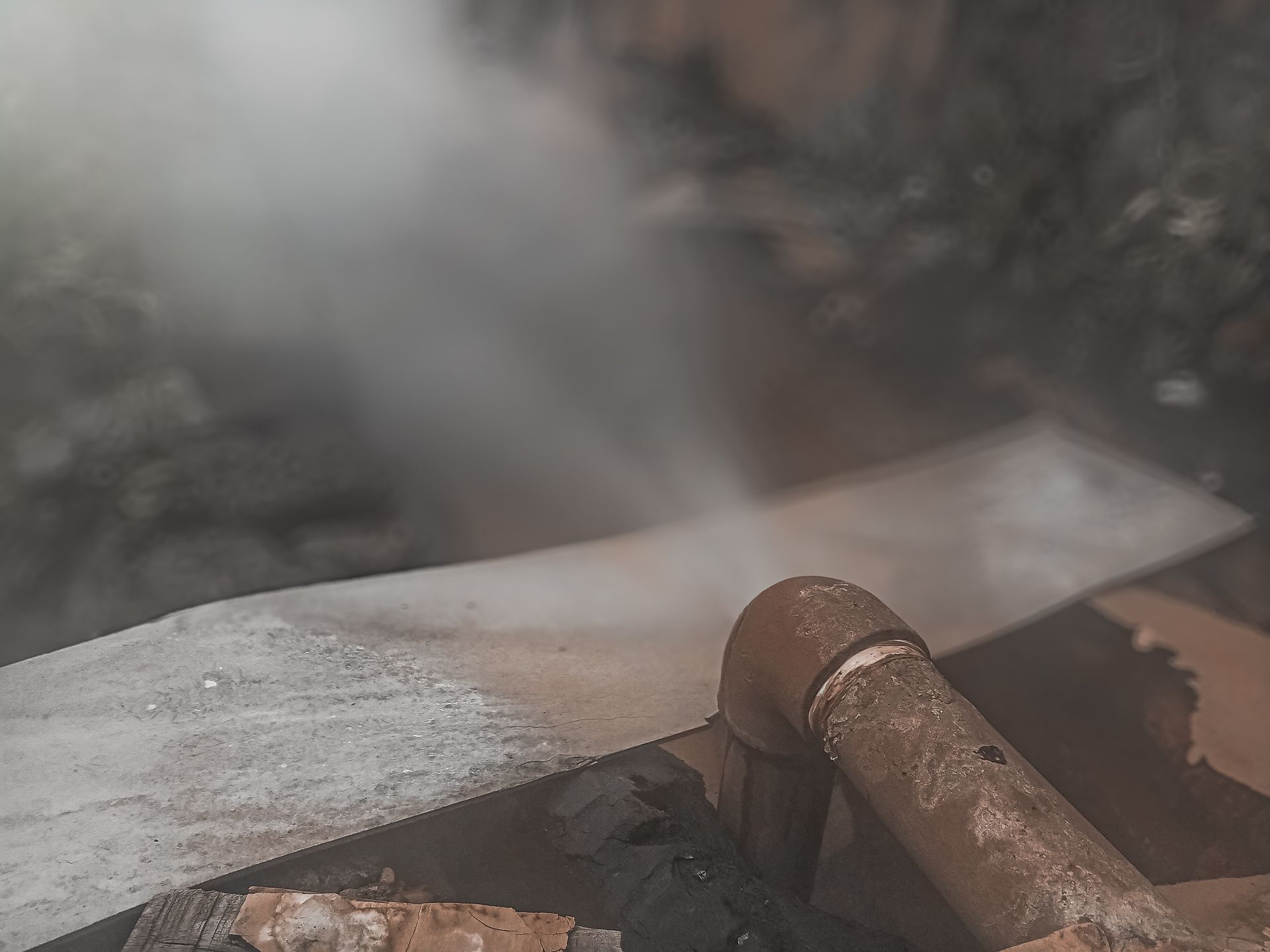 Steam rising over a metal pipe in a rocky industrial setting