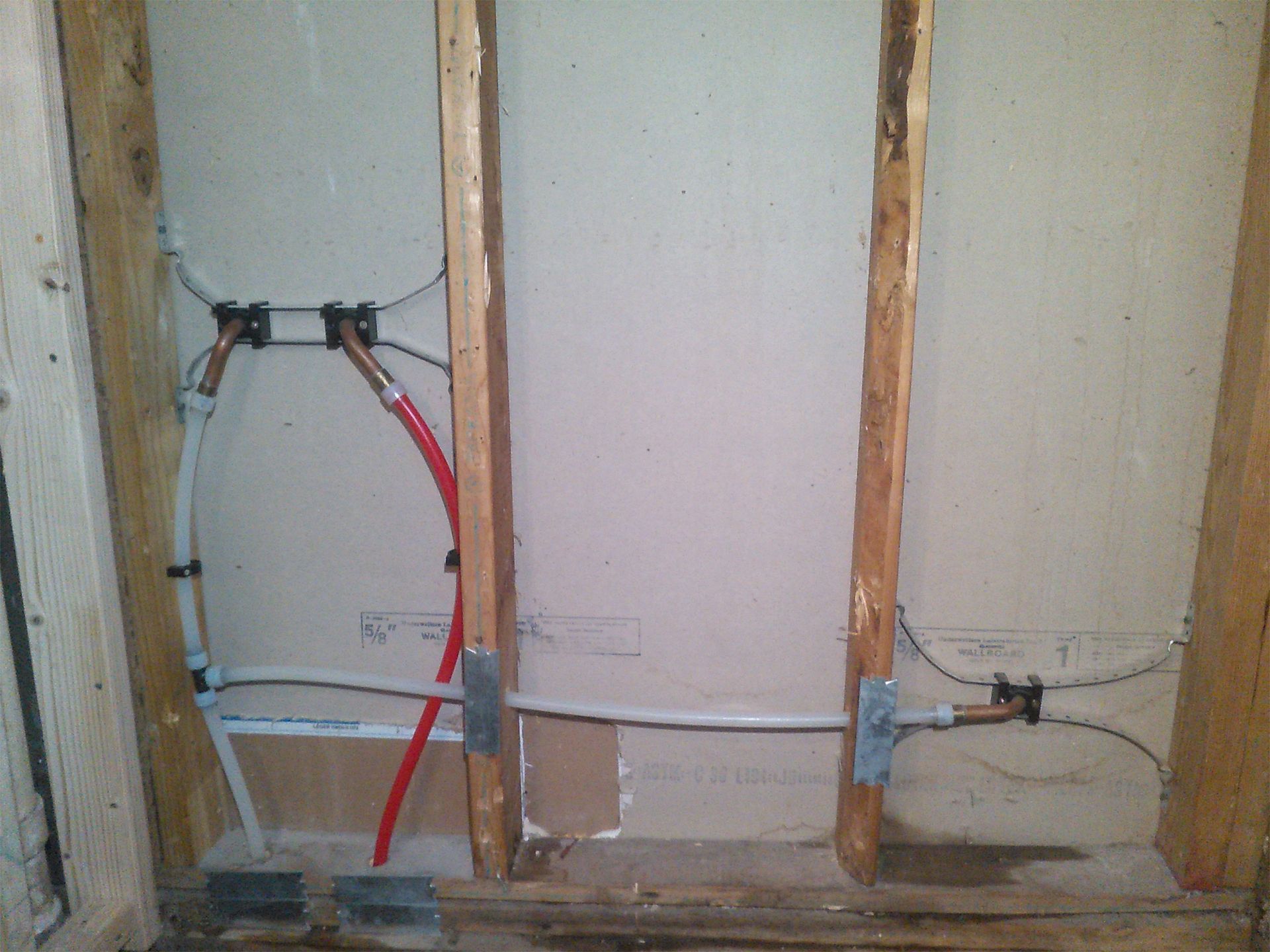 Exposed wall framing with plumbing and electrical lines in a renovation area.