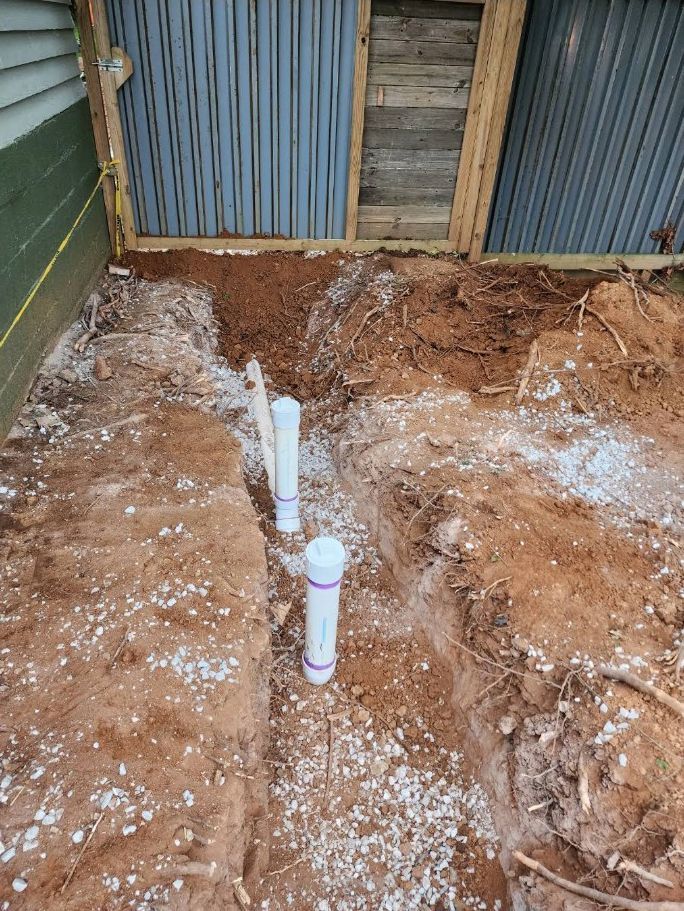 Two white PVC pipes protrude from a dirt excavation beside a corrugated metal wall.