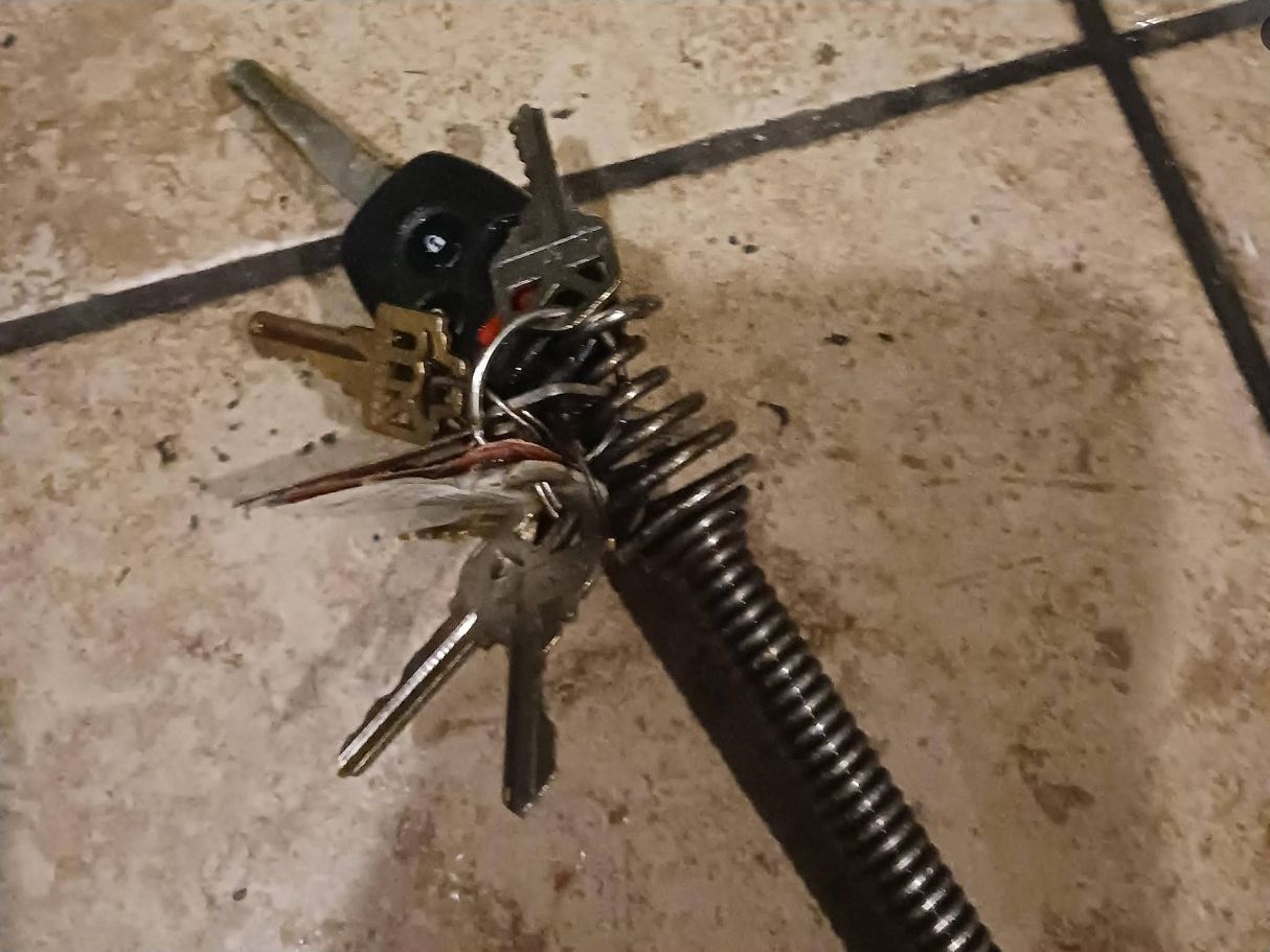 Metal tool keychain with several keys and a black round attachment lying on a tiled floor.