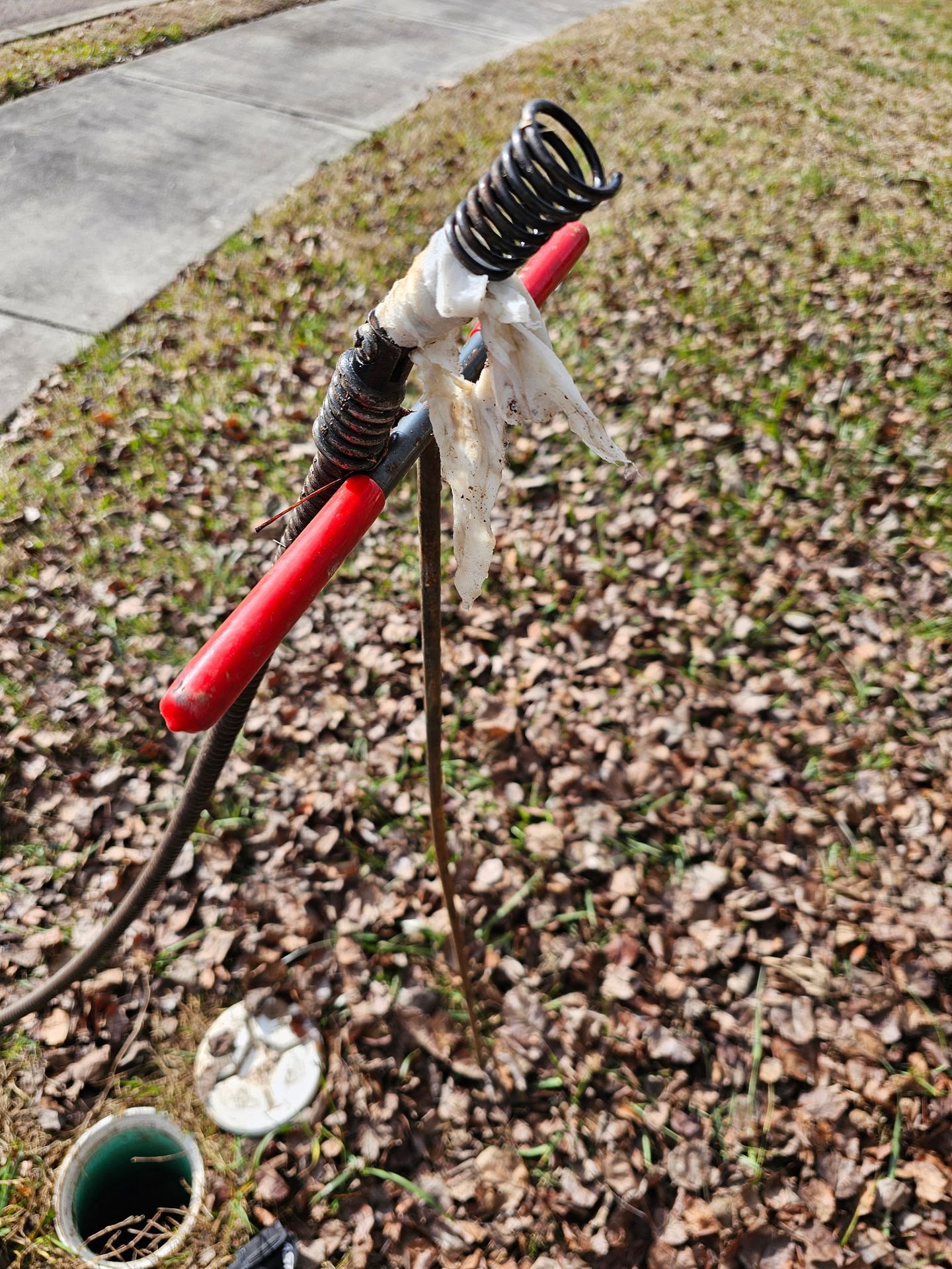 Red-handled survey tripod mounted with a black spring-like coil on a grassy roadside beside a path.
