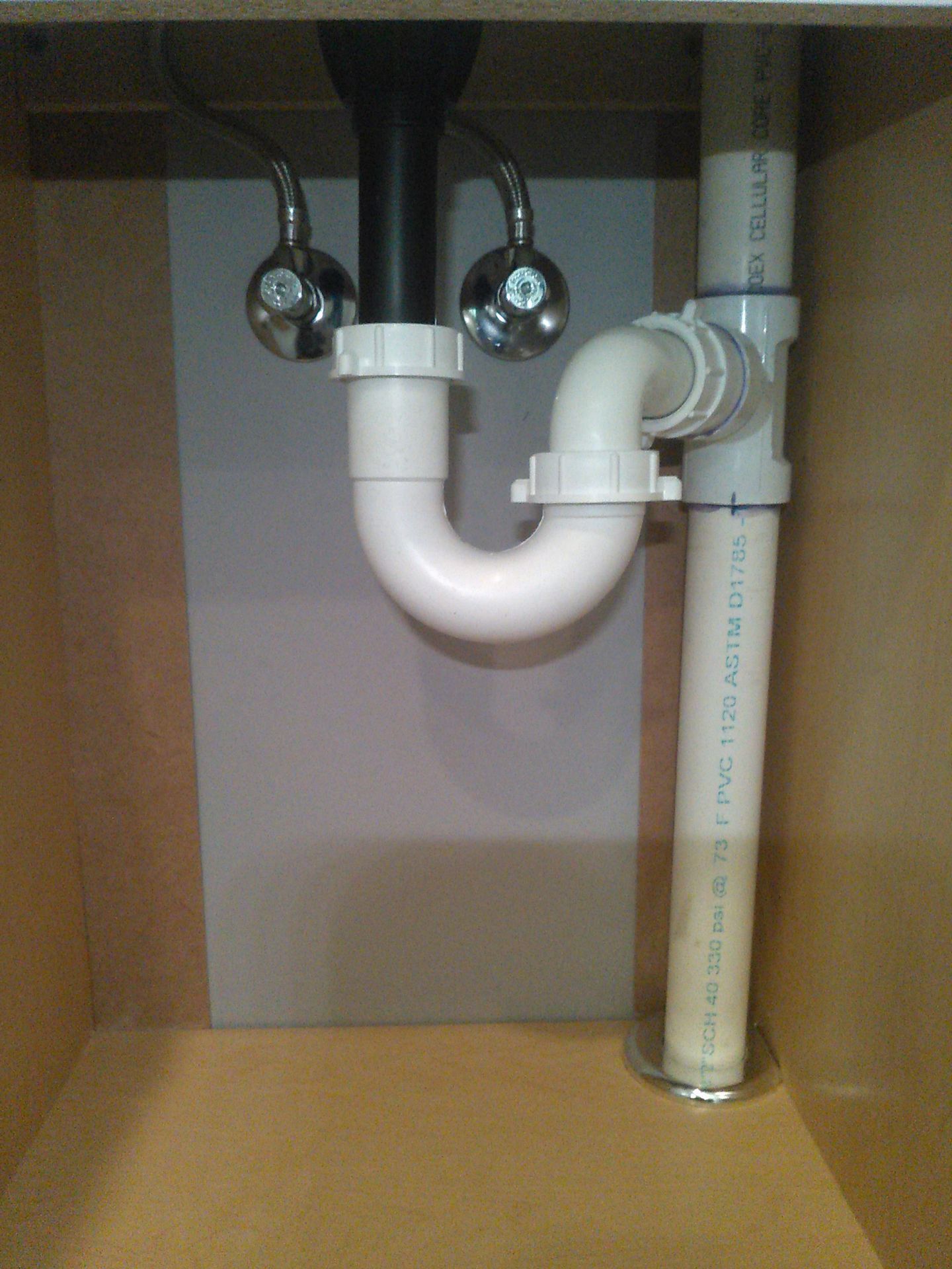 Under-sink plumbing with white PVC drain pipes and a P-trap inside a cabinet