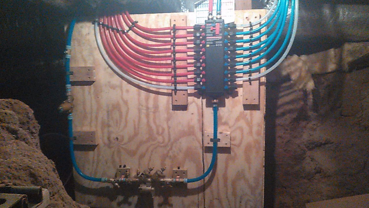 Electrical panel with neatly bundled red and blue wires mounted on plywood in an unfinished wall cavity.