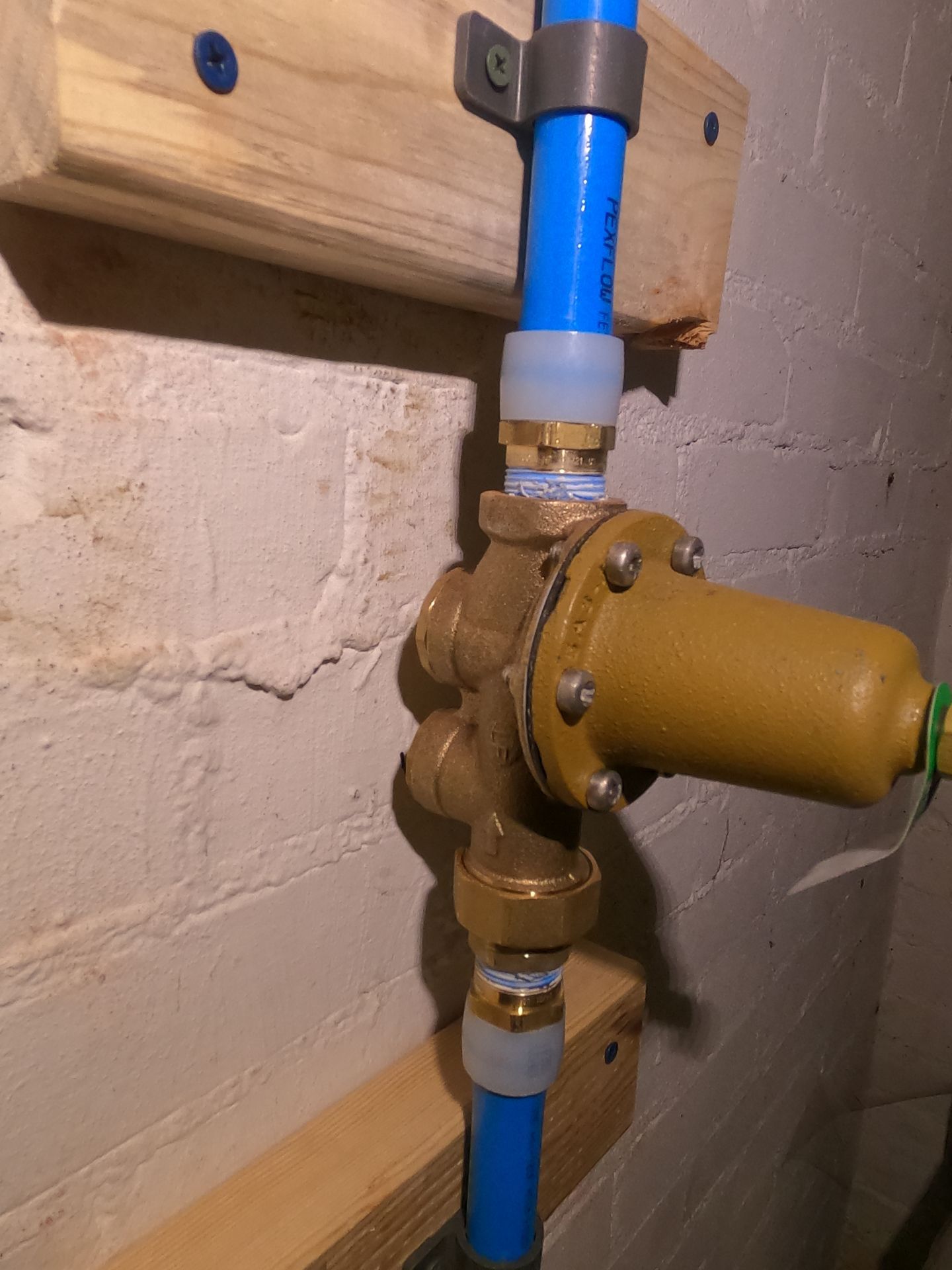 Blue pipes connected to a brass valve on a basement wall