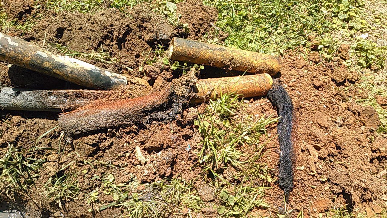 Several blackened garden hoses or pipes lying on dirt and grass, one charred and broken