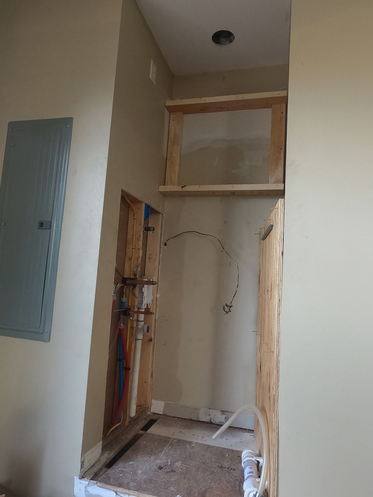 Partially finished closet opening with exposed framing, wiring, and electrical panel in a beige hallway