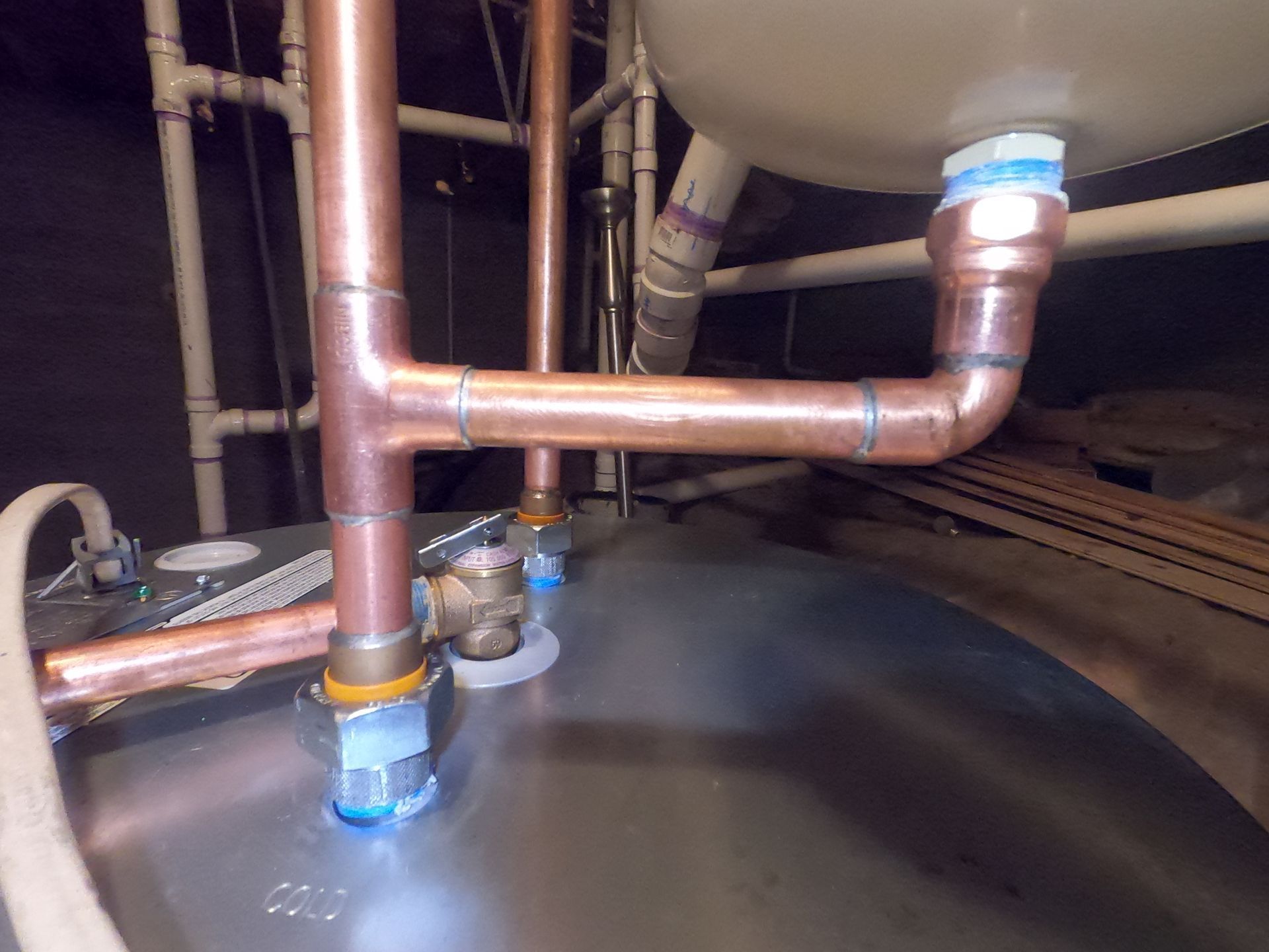 Copper pipes and fittings above a metal tank, with a blue-lit valve in an industrial setting