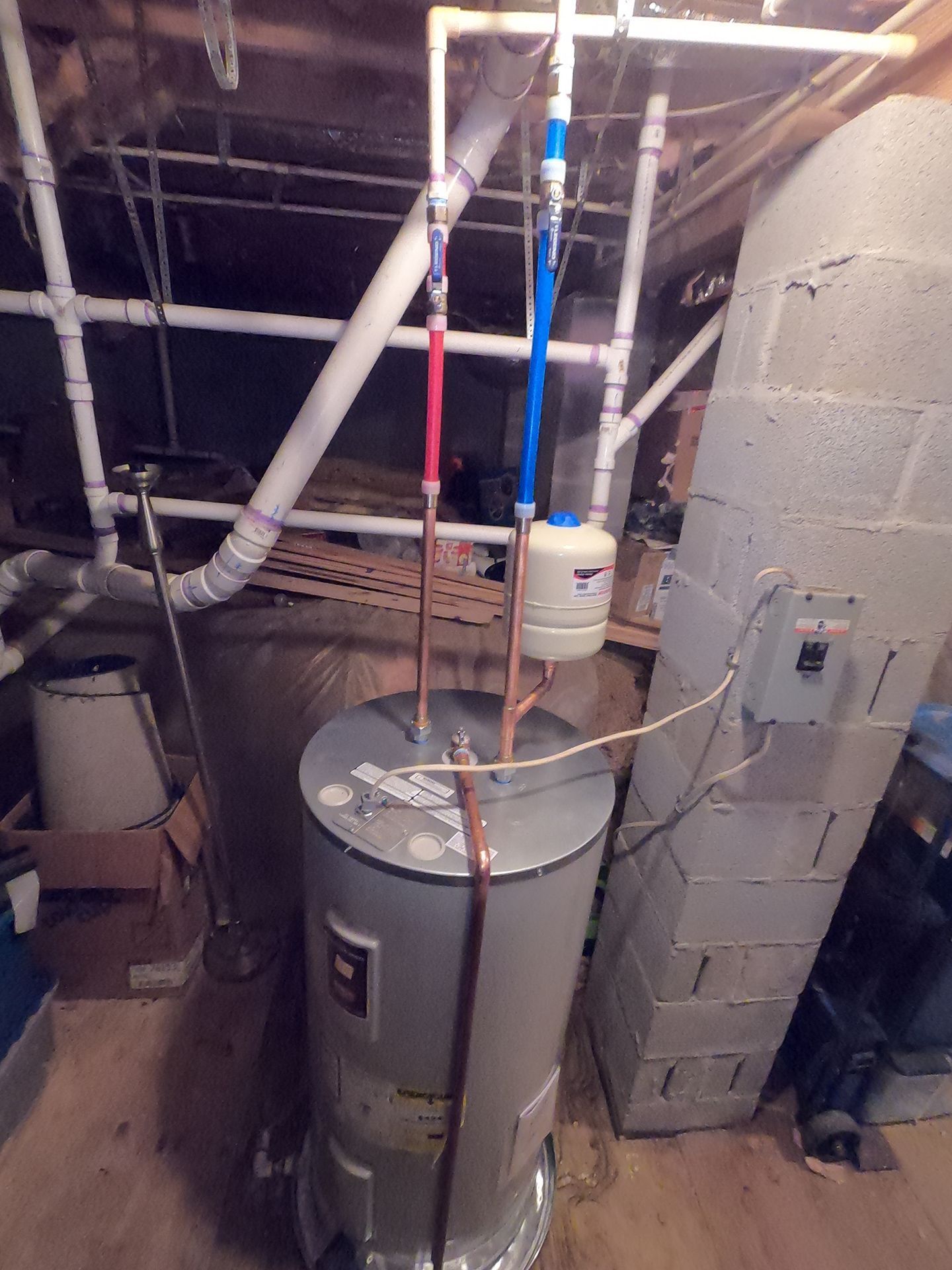 Water heater with exposed pipes and wiring in a utility basement room.