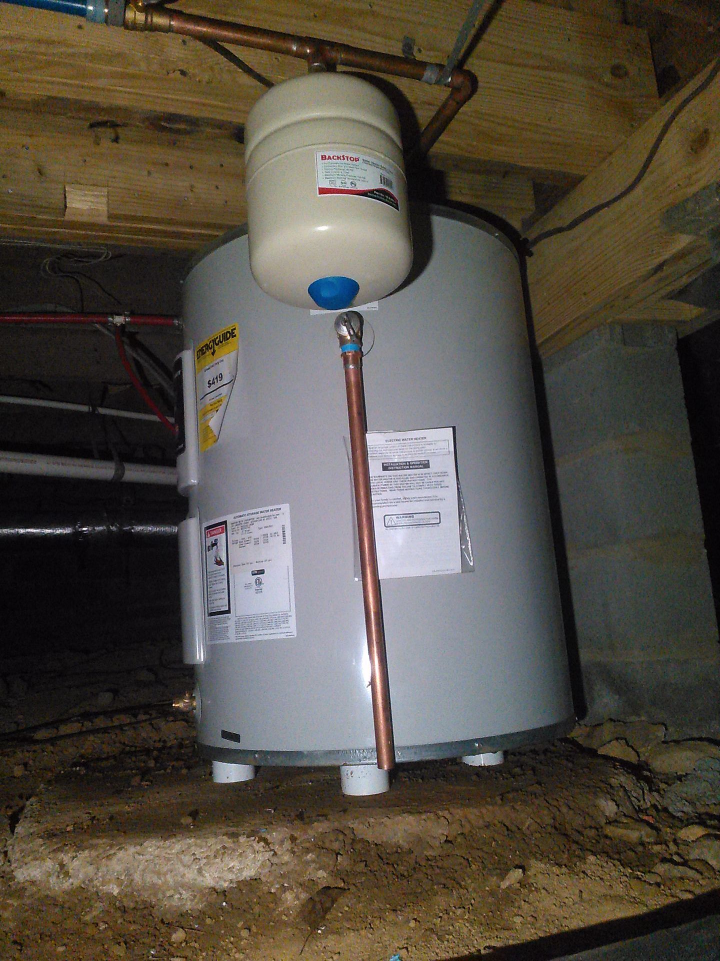 Gray water heater in a basement, with a white expansion tank and copper pipe under wooden beams.