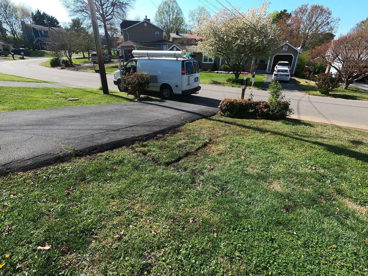 White utility truck parked beside a driveway in a suburban neighborhood on a sunny day