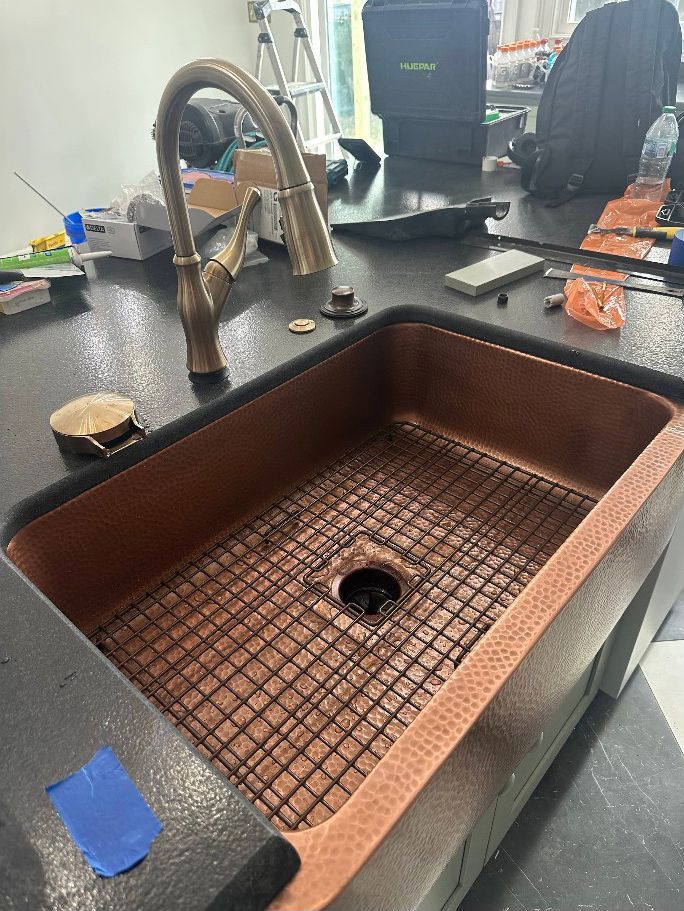Copper farmhouse sink with a black countertop and chrome faucet in a kitchen.