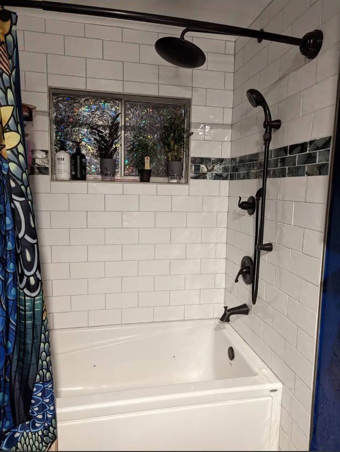 White-tiled shower with black fixtures, a blue patterned curtain, and a built-in tub.