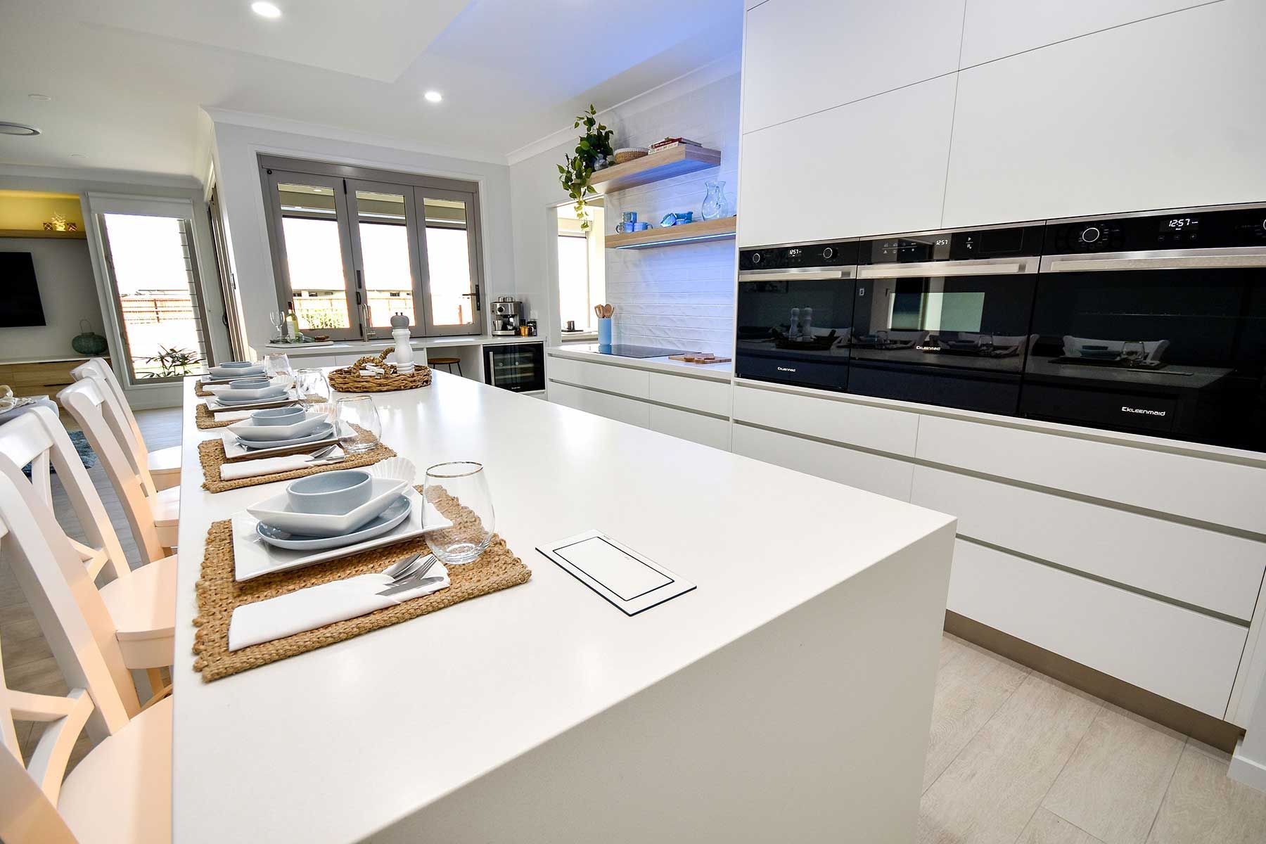 Modern White Kitchen with Long Island, Set Tables, and Glossy Black Backsplash — Bundy Homes in Bundaberg North, QLD