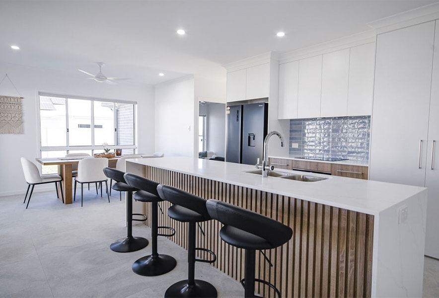 Bright White Kitchen with Island, Bar Stools, and Dining Table — Bundy Homes in Bundaberg North, QLD