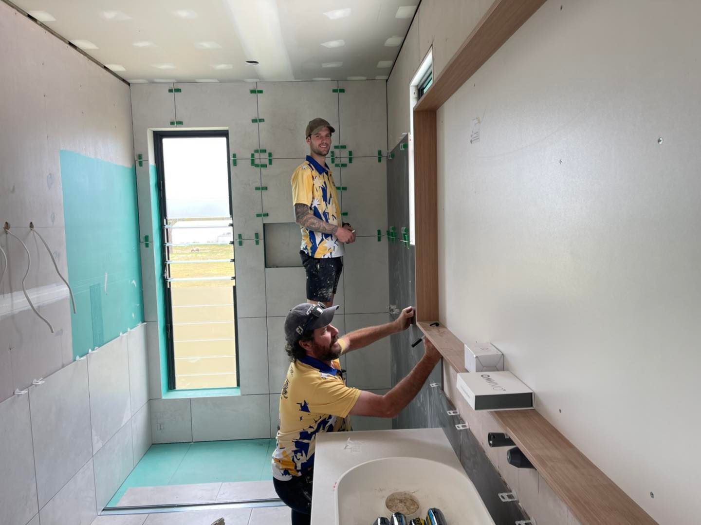 Workers Installing a Mirror in A Narrow Bathroom Hallway — Bundy Homes in Bundaberg North, QLD