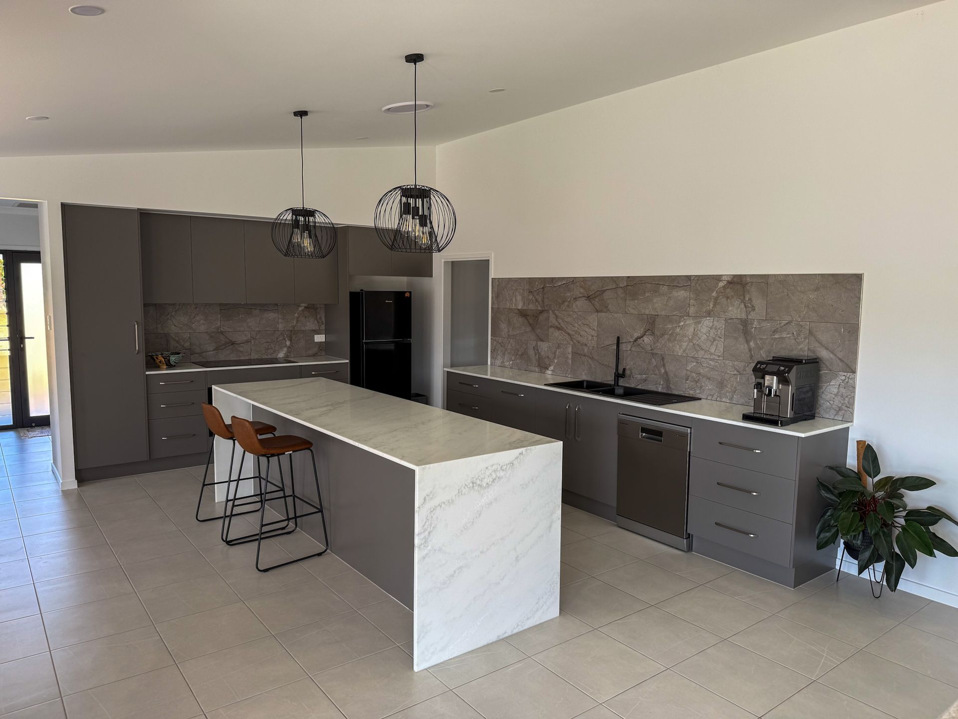 Modern kitchen with white island, gray cabinets, stone backsplash, and pendant lights