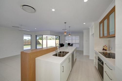 Modern White Kitchen with Island, Wood Accents, and Large Windows — Bundy Homes in Bundaberg North, QLD