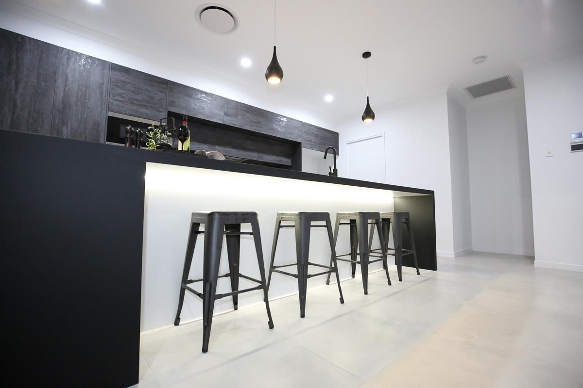 Modern Kitchen with Black Island, Four Stools, and Hanging Pendant Lights — Bundy Homes in Bundaberg North, QLD